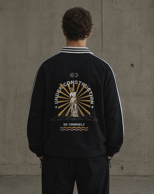 Person wearing a black jacket with a graphic design on the back against a concrete wall. Stylist streetwear collar Sweatshirt, comfy formal collar Sweatshirt, fashion collar Sweatshirt, graphic collar Sweatshirt