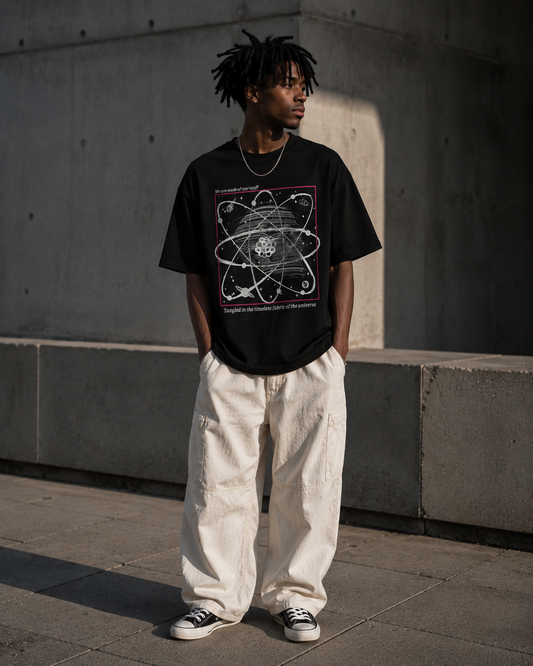 Person wearing a black t-shirt with a graphic design, standing against a concrete wall. Stylist streetwear tee, comfy formal tee, fashion tee, graphic tee