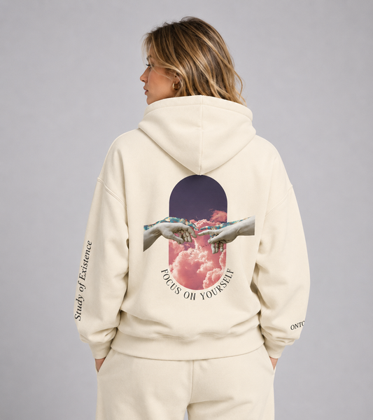 Person wearing a beige hoodie with a graphic design on the back, standing against a plain background. Stylist streetwear hoodie, comfy formal hoodie, fashion hoodie, graphic hoodie, no front pocket hoodie, large hooded hoodie, large hood hoodie, oversized hoodie