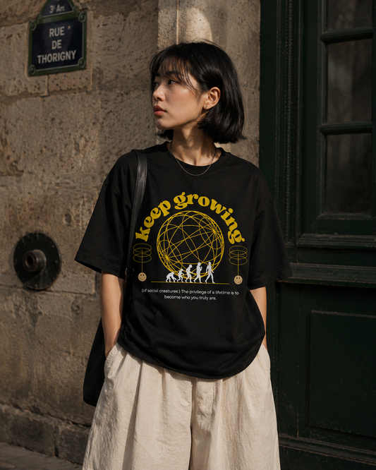 Person wearing a black t-shirt with yellow text and graphics in an urban setting. Stylist streetwear tee, comfy formal tee, fashion tee, graphic tee