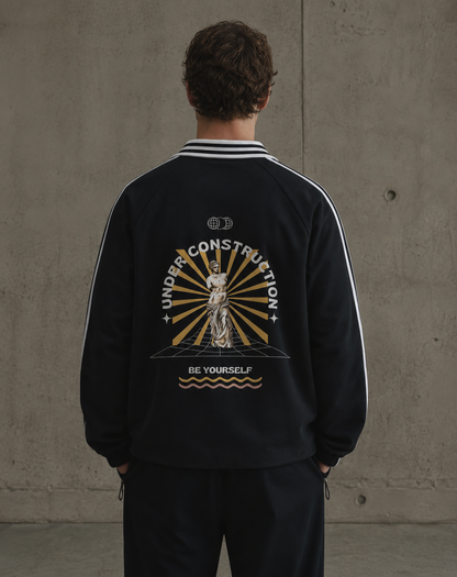 Person wearing a black jacket with a graphic design on the back against a concrete wall. Stylist streetwear collar Sweatshirt, comfy formal collar Sweatshirt, fashion collar Sweatshirt, graphic collar Sweatshirt