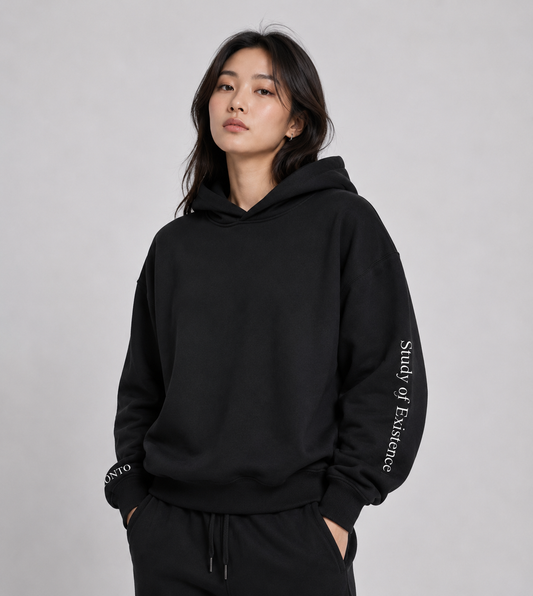 Person wearing a black hoodie with text on sleeves against a gray background.Stylist streetwear hoodie, comfy formal hoodie, fashion hoodie, graphic hoodie, no front pocket hoodie, large hooded hoodie, large hood hoodie, oversized hoodie