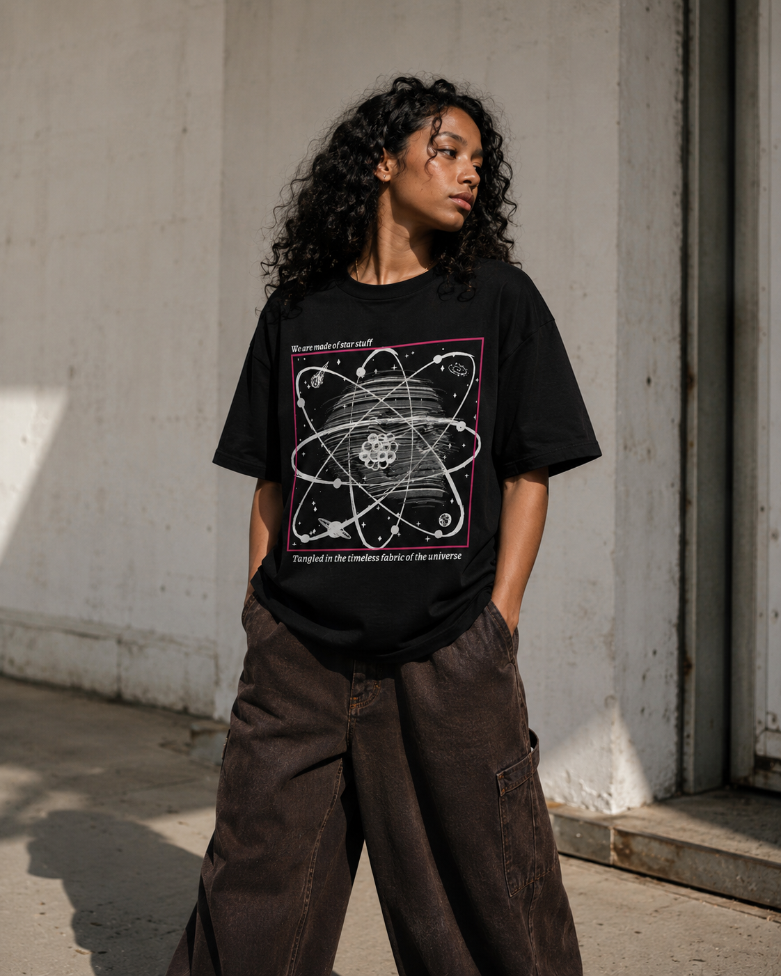Person wearing a black t-shirt with a graphic design, standing against a concrete wall. Stylist streetwear tee, comfy formal tee, fashion tee, graphic tee
