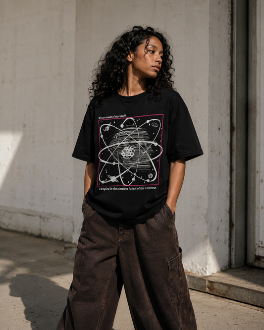 Person wearing a black t-shirt with a graphic design, standing against a concrete wall. Stylist streetwear tee, comfy formal tee, fashion tee, graphic tee
