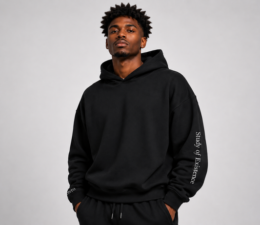 Man wearing a black hoodie with text on sleeves against a gray background. Stylist streetwear hoodie, comfy formal hoodie, fashion hoodie, graphic hoodie, no front pocket hoodie, large hooded hoodie, large hood hoodie, oversized hoodie
