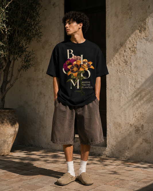 Person wearing a black t-shirt with floral design and text, standing outdoors against a textured wall. Stylist streetwear tee, comfy formal tee, fashion tee, graphic tee
