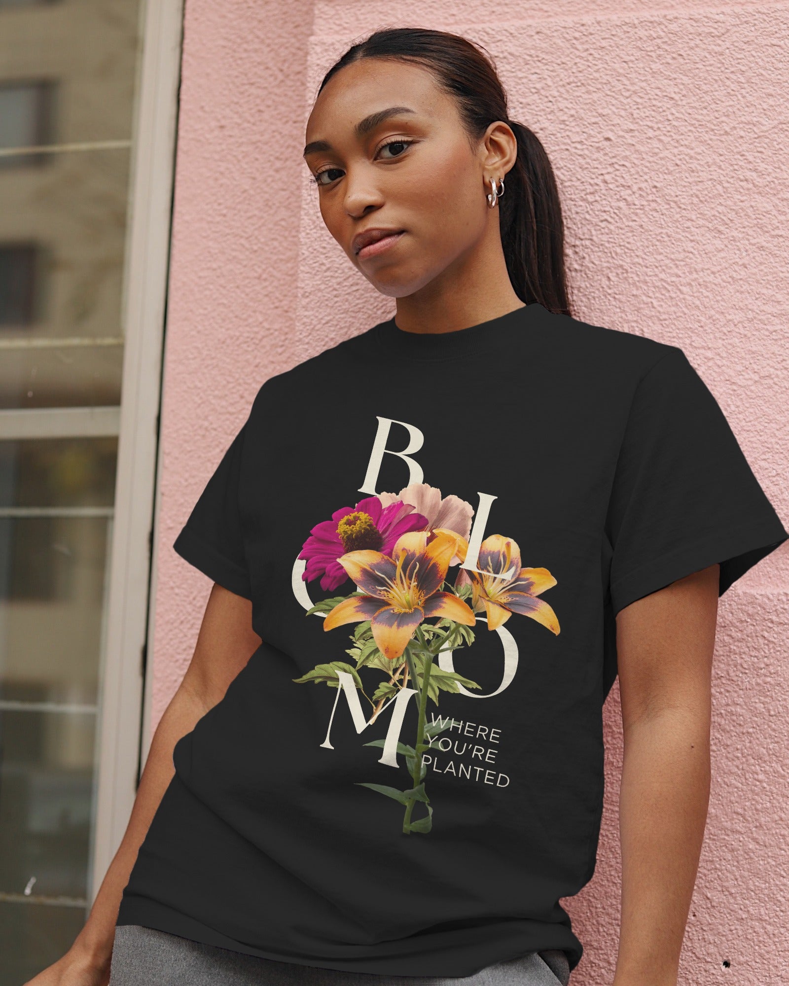Woman wearing a black t-shirt with floral design and text against a pink wall.