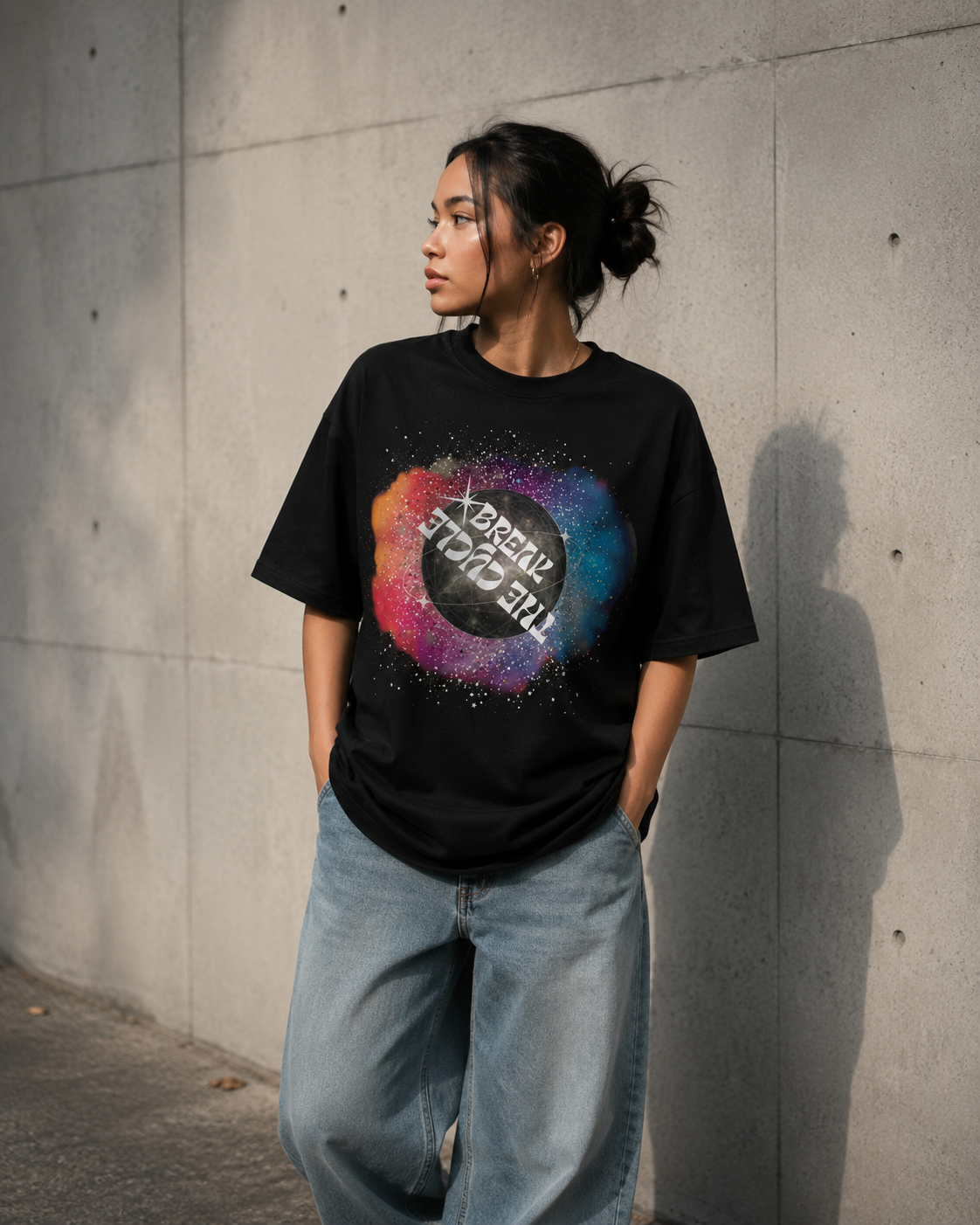 Person wearing a black t-shirt with a colorful graphic design against a concrete wall. Stylist streetwear tee, comfy formal tee, fashion tee, graphic tee