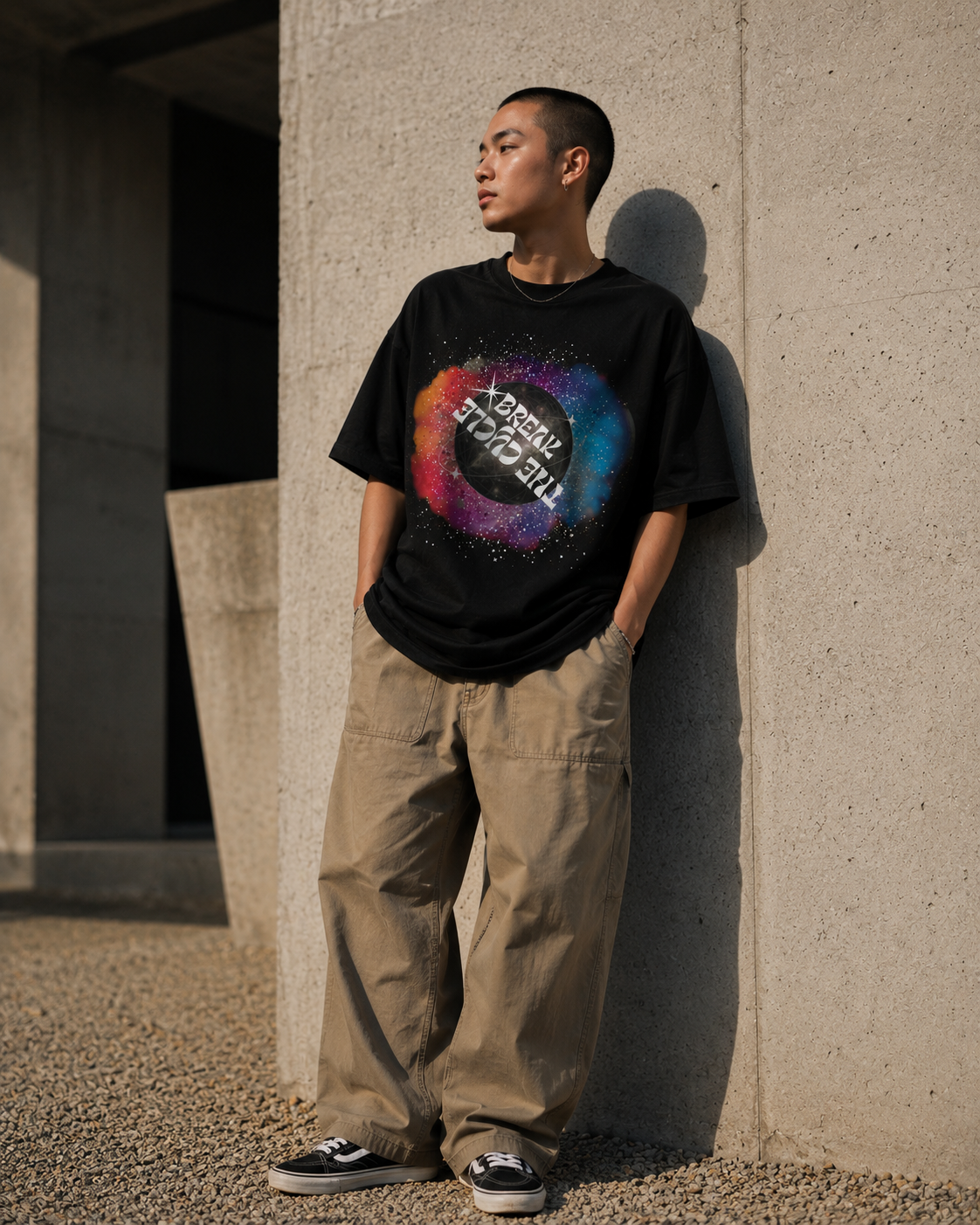 Person wearing a black t-shirt with a colorful graphic design, standing against a concrete wall. Stylist streetwear tee, comfy formal tee, fashion tee, graphic tee