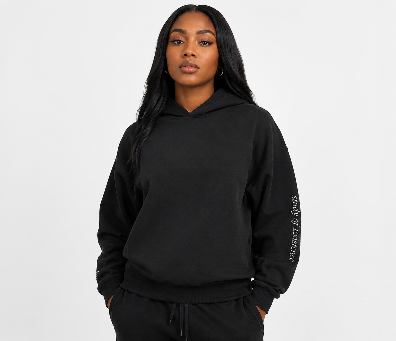 Person wearing a black hoodie with text on sleeve against a white background. Stylist streetwear hoodie, comfy formal hoodie, fashion hoodie, graphic hoodie, no front pocket hoodie, large hooded hoodie, large hood hoodie, oversized hoodie.