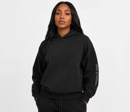 Person wearing a black hoodie with text on sleeve against a white background. Stylist streetwear hoodie, comfy formal hoodie, fashion hoodie, graphic hoodie, no front pocket hoodie, large hooded hoodie, large hood hoodie, oversized hoodie.