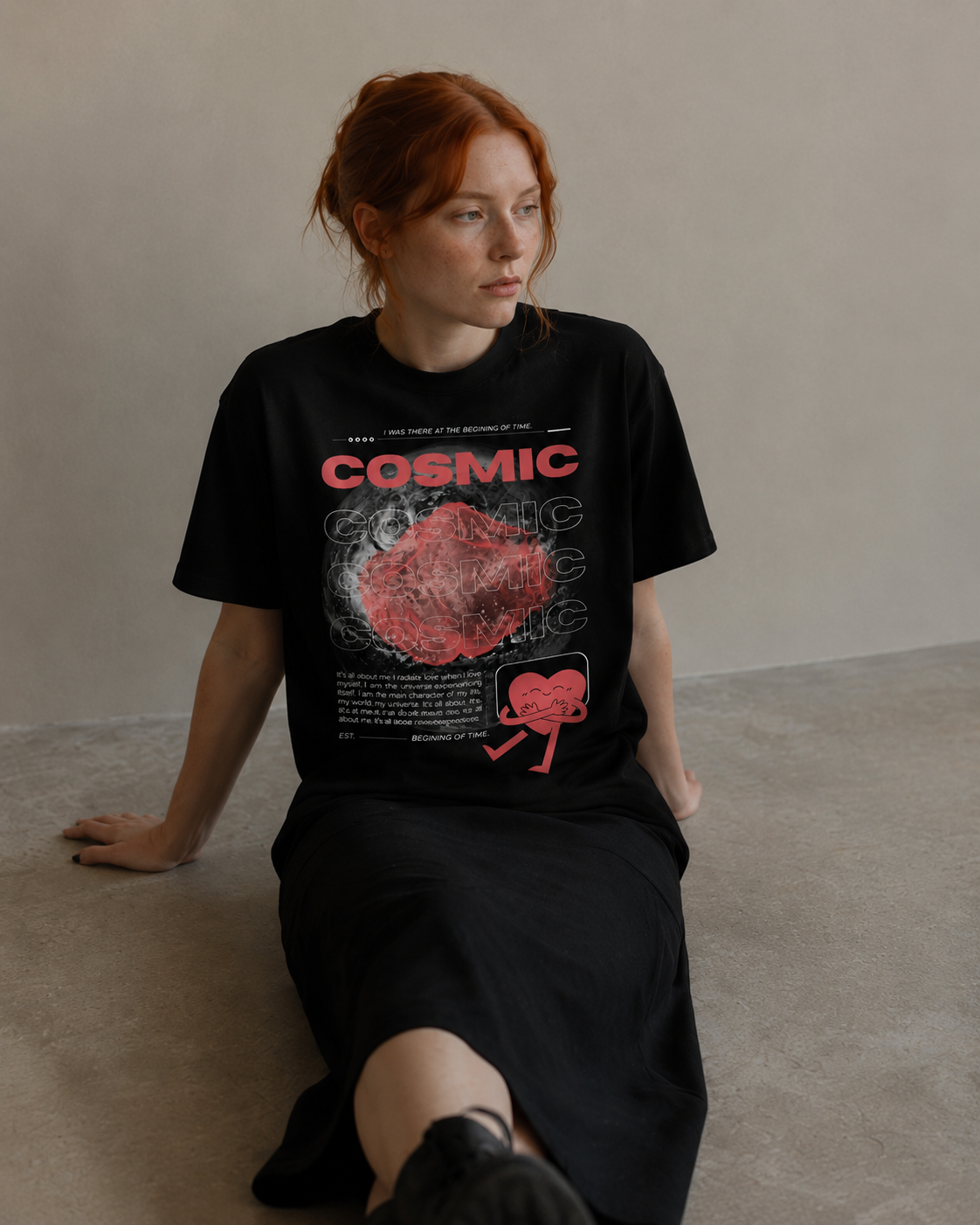 Person wearing a black t-shirt with 'Cosmic' design sitting on a plain background. Stylist streetwear tee, comfy formal tee, fashion tee, graphic tee
