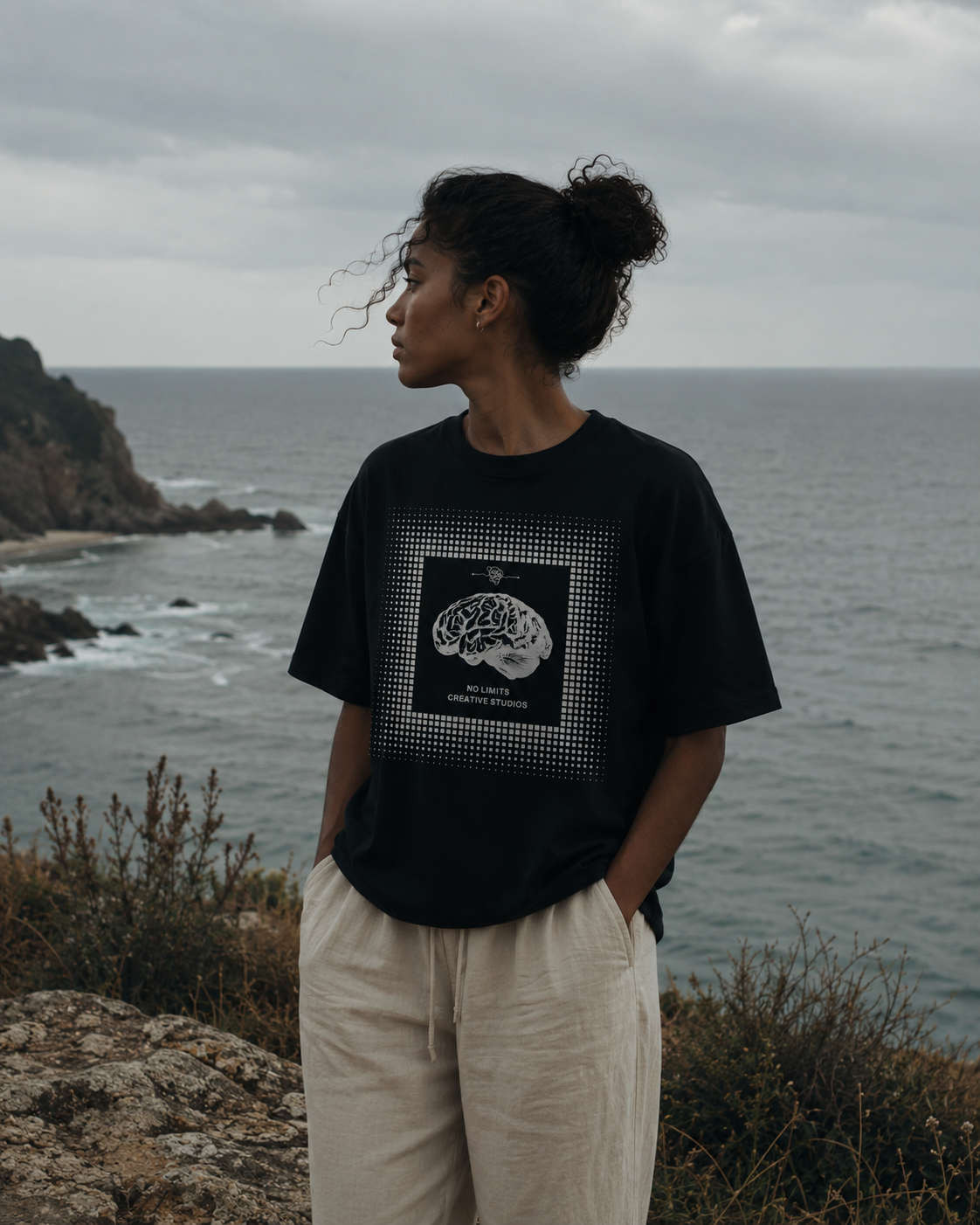 Person wearing a black t-shirt with a graphic design standing on a coastal cliff. Stylist streetwear tee, comfy formal tee, fashion tee, graphic tee