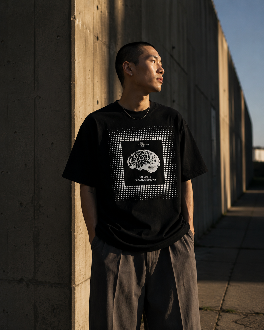 Person wearing a black t-shirt with a graphic design, standing against a concrete wall. Stylist streetwear tee, comfy formal tee, fashion tee, graphic tee