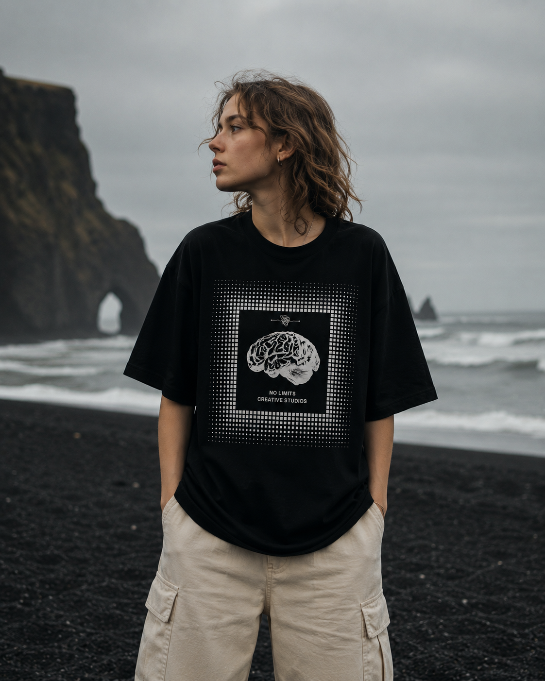 Person wearing a black t-shirt with a graphic design on a black sand beach. Stylist streetwear tee, comfy formal tee, fashion tee, graphic tee