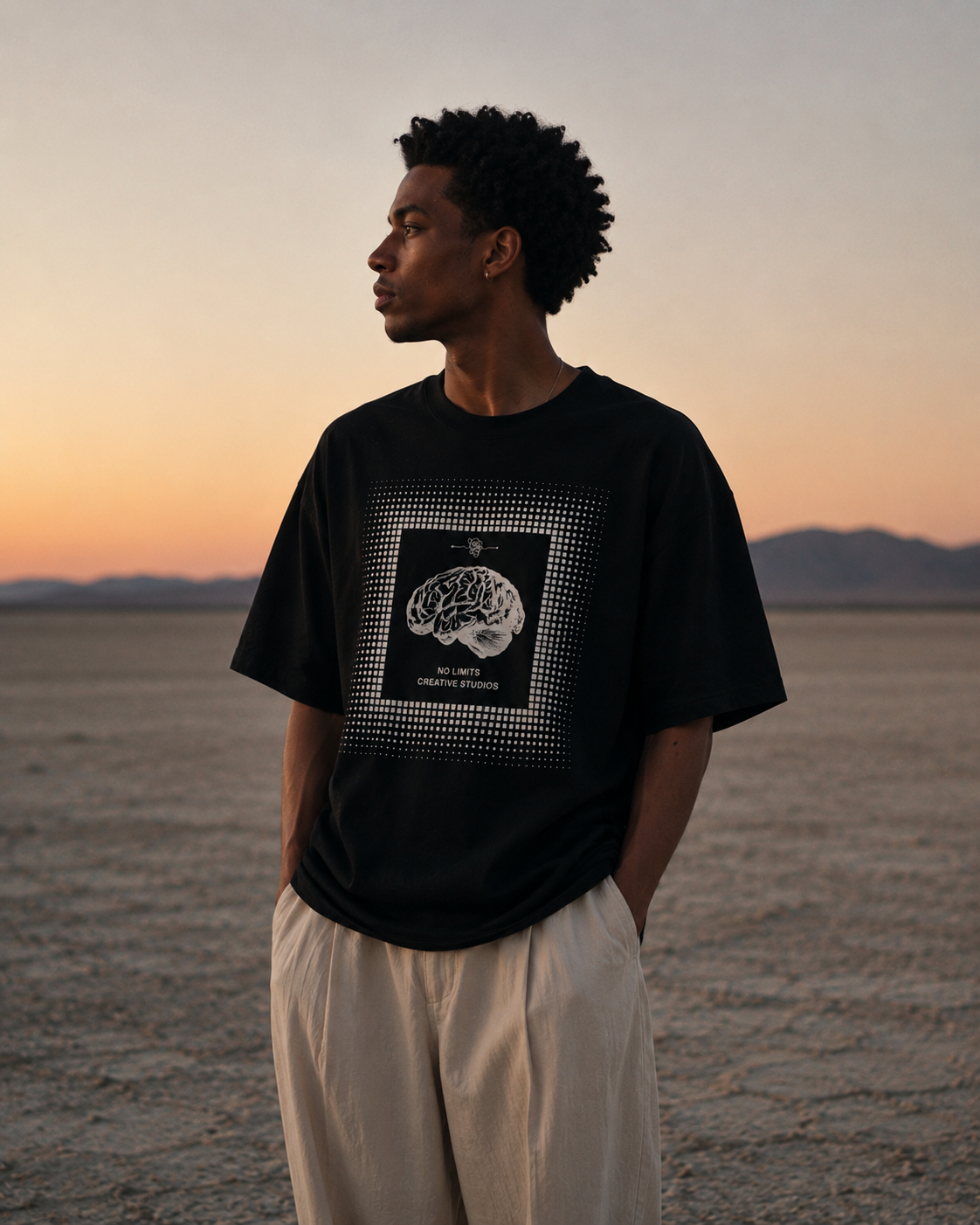 Person wearing a black t-shirt with a graphic design in a desert landscape at sunset. Stylist streetwear tee, comfy formal tee, fashion tee, graphic tee