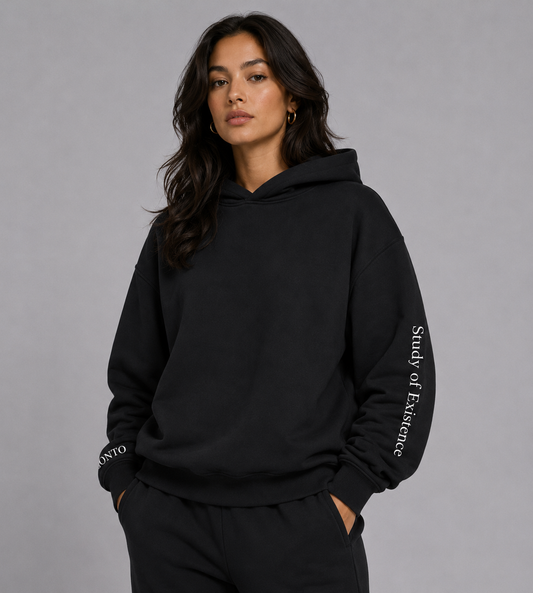 Person wearing a black hoodie with text on sleeves against a gray background. Stylist streetwear hoodie, comfy formal hoodie, fashion hoodie, graphic hoodie, no front pocket hoodie, large hooded hoodie, large hood hoodie, oversized hoodie