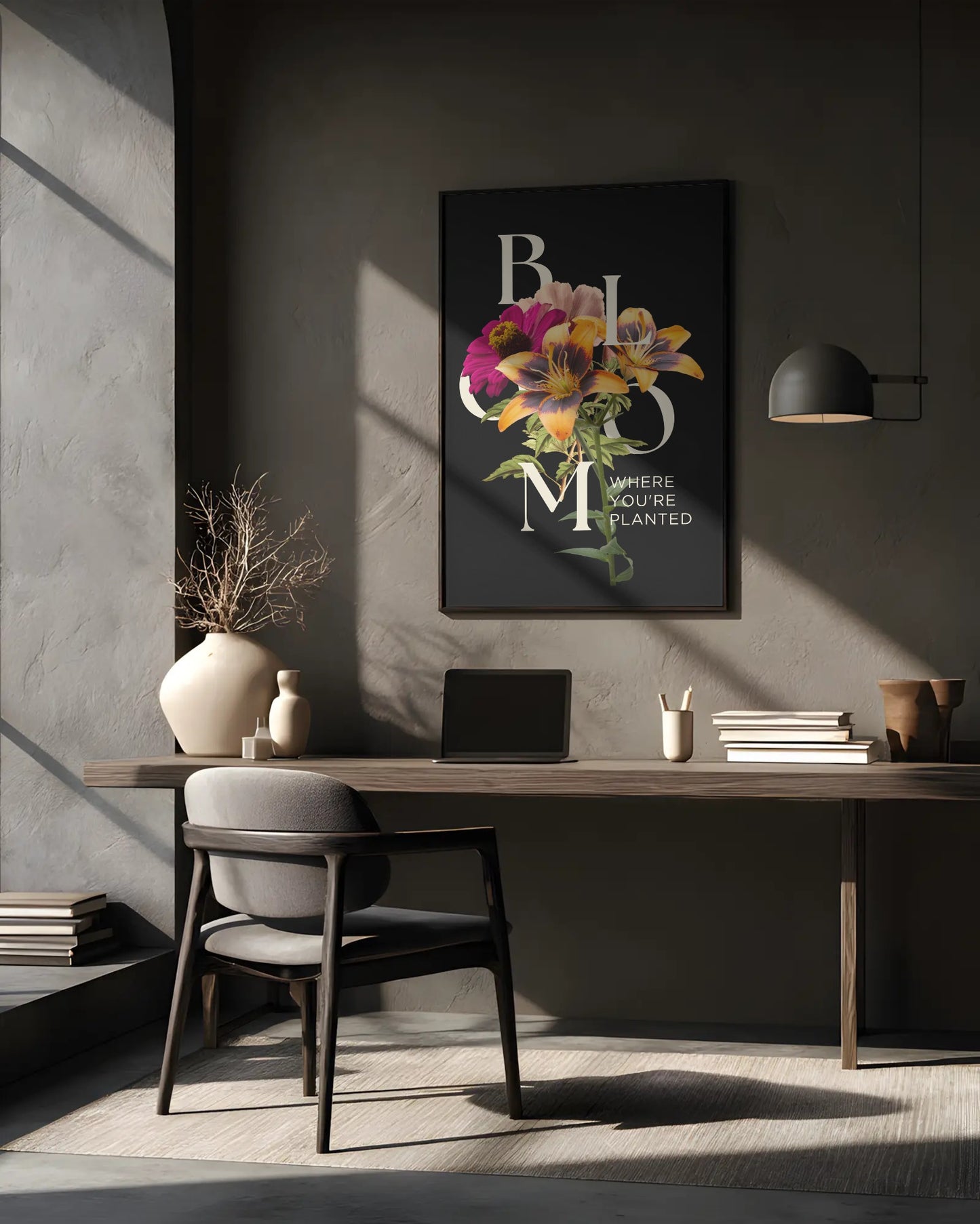 Modern office desk with a laptop, books, and decorative items against a gray wall with a framed floral print.