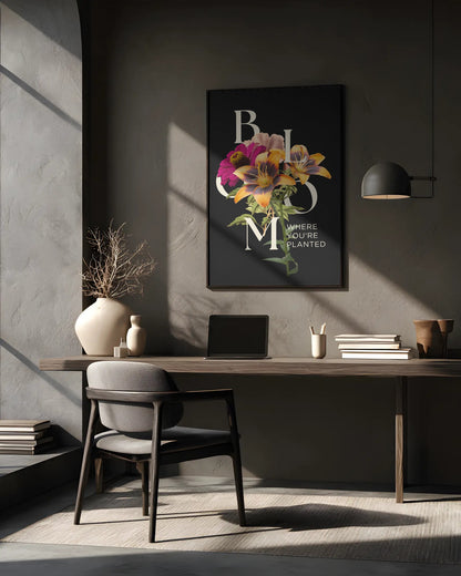 Modern office desk with a laptop, books, and decorative items against a gray wall with a framed floral print.
