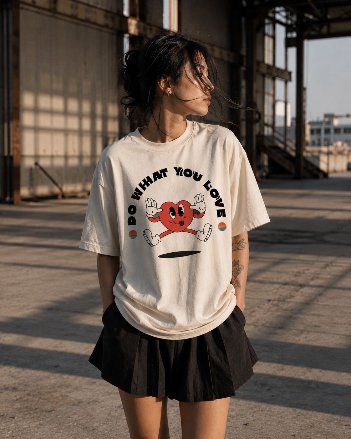 Person wearing a white t-shirt with a graphic design and text, standing in an industrial setting. Stylist streetwear tee, comfy formal tee, fashion tee, graphic tee