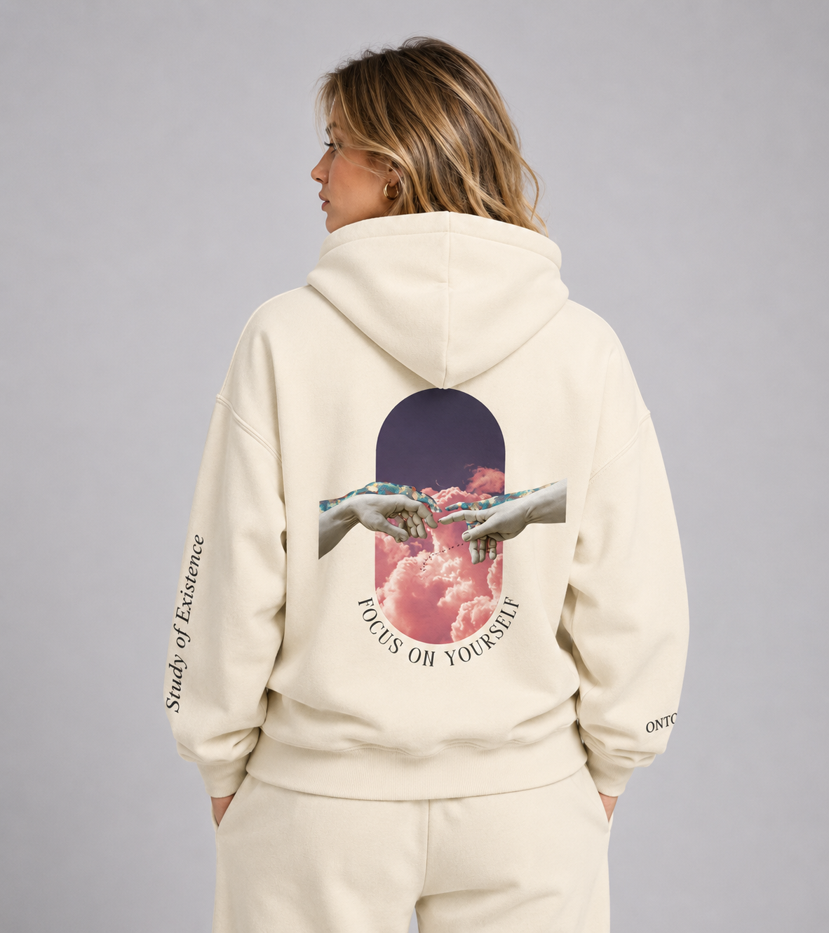 Person wearing a beige hoodie with a graphic design on the back, standing against a plain background. Stylist streetwear hoodie, comfy formal hoodie, fashion hoodie, graphic hoodie, no front pocket hoodie, large hooded hoodie, large hood hoodie, oversized hoodie
