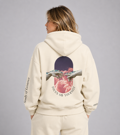 Person wearing a beige hoodie with a graphic design on the back, standing against a plain background. Stylist streetwear hoodie, comfy formal hoodie, fashion hoodie, graphic hoodie, no front pocket hoodie, large hooded hoodie, large hood hoodie, oversized hoodie