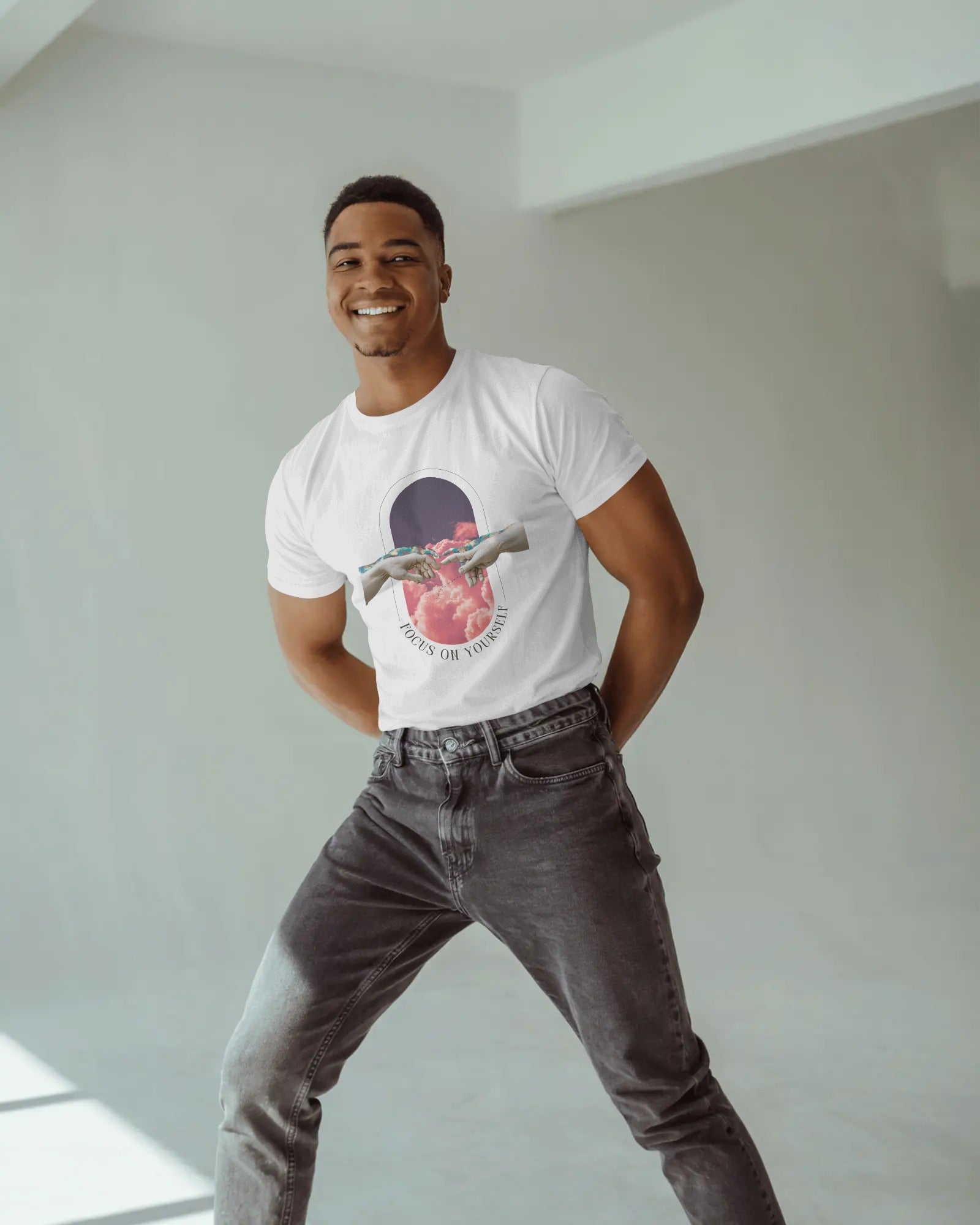 Man wearing a white t-shirt with a graphic design and dark jeans standing in a well-lit room.