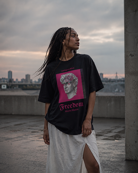Person wearing a black t-shirt with a graphic design and text, standing on a rooftop with a cityscape in the background. Stylist streetwear tee, comfy formal tee, fashion tee, graphic tee