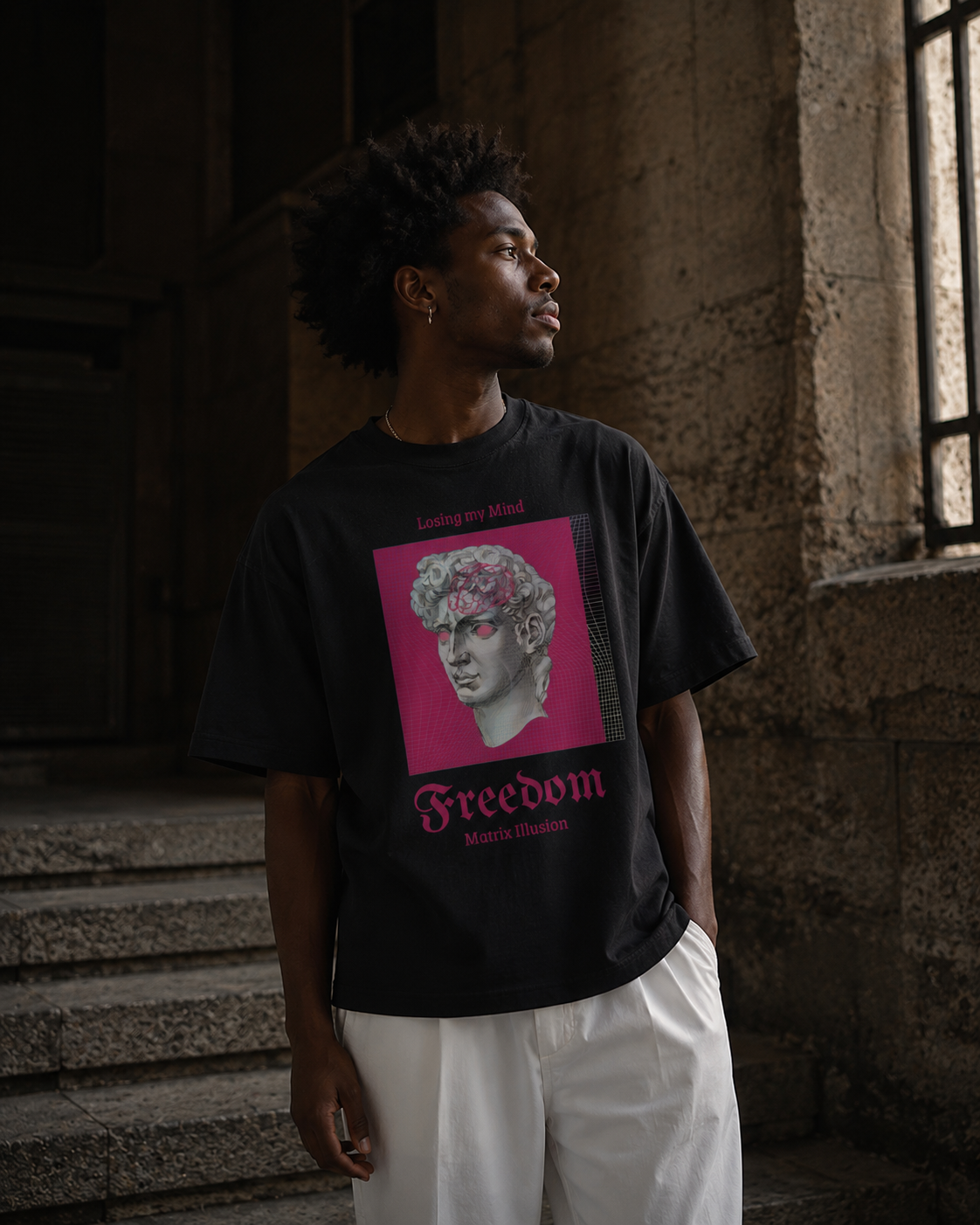 Person wearing a black t-shirt with a graphic design and text, standing in a stone building. Stylist streetwear tee, comfy formal tee, fashion tee, graphic tee