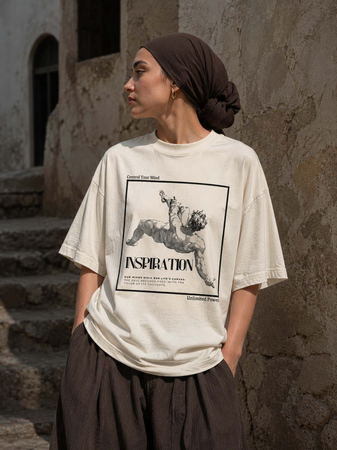 Person wearing a white t-shirt with a graphic design and text, standing against a textured wall. Stylist streetwear tee, comfy formal tee, fashion tee, graphic tee