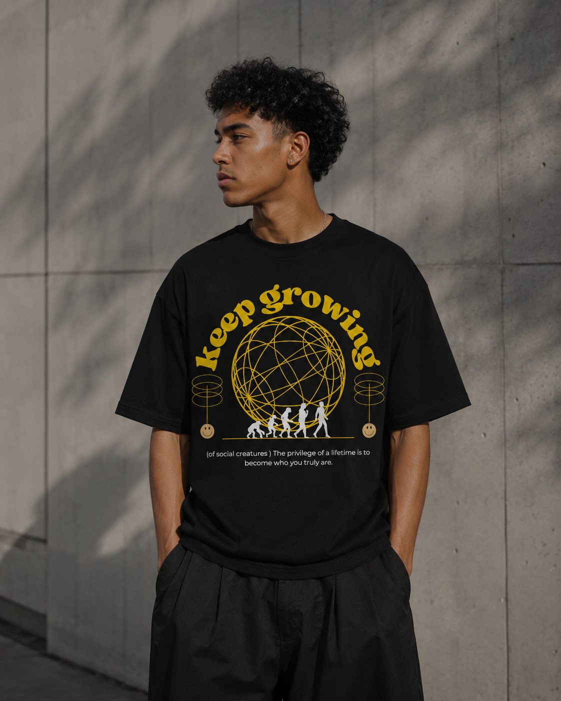 Person wearing a black t-shirt with 'keep growing' graphic design against a gray wall. Stylist streetwear tee, comfy formal tee, fashion tee, graphic tee