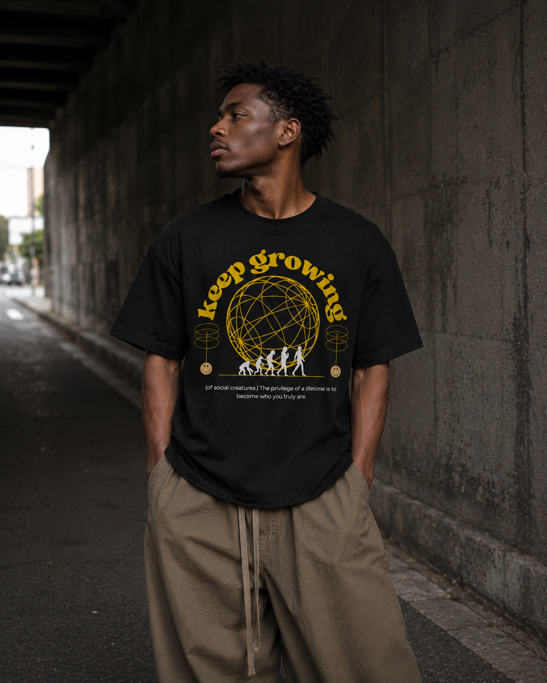 Man wearing a black t-shirt with 'keep growing' text and graphic, standing against a concrete wall. Stylist streetwear tee, comfy formal tee, fashion tee, graphic tee