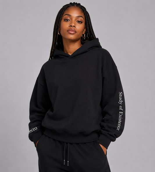 Person wearing a black hoodie with text on sleeves against a gray background. Stylist streetwear hoodie, comfy formal hoodie, fashion hoodie, graphic hoodie, no front pocket hoodie, large hooded hoodie, large hood hoodie, oversized hoodie