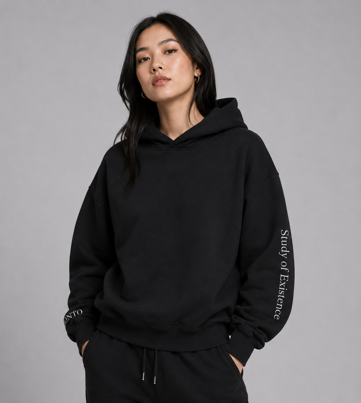 Person wearing a black hoodie with text on sleeve against a gray background. Stylist streetwear hoodie, comfy formal hoodie, fashion hoodie, graphic hoodie, no front pocket hoodie, large hooded hoodie, large hood hoodie, oversized hoodie