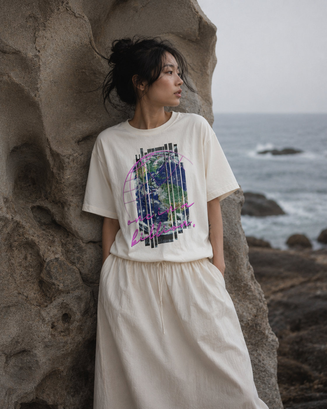 Woman wearing a white t-shirt with a colorful graphic design, standing on a rocky beach. Stylist streetwear tee, comfy formal tee, fashion tee, graphic tee