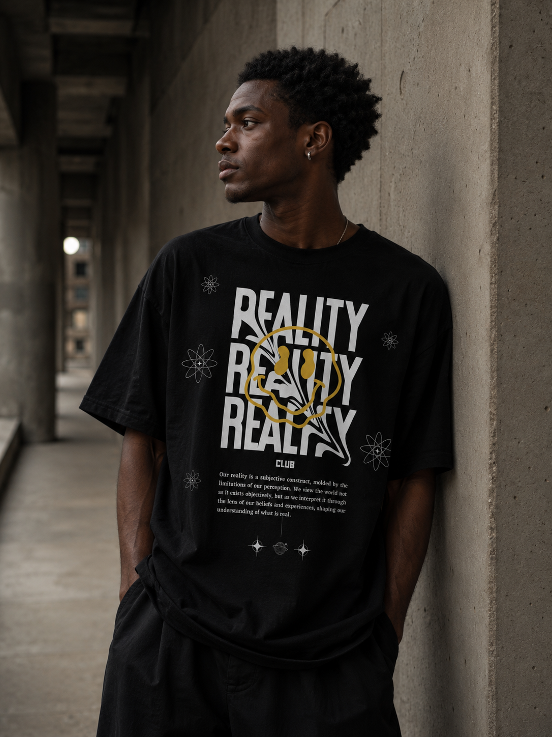 Person wearing a black t-shirt with 'REALITY CLUB' text design, standing against a concrete wall. Stylist streetwear tee, comfy formal tee, fashion tee, graphic tee