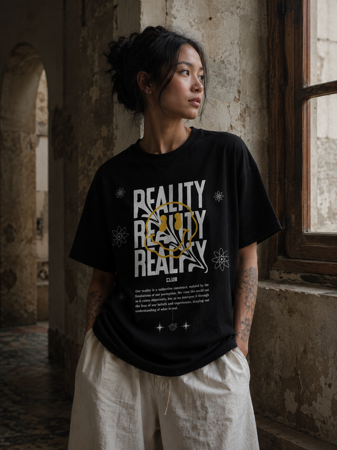 Person wearing a black t-shirt with 'REALITY' text in a dilapidated building. Stylist streetwear tee, comfy formal tee, fashion tee, graphic tee