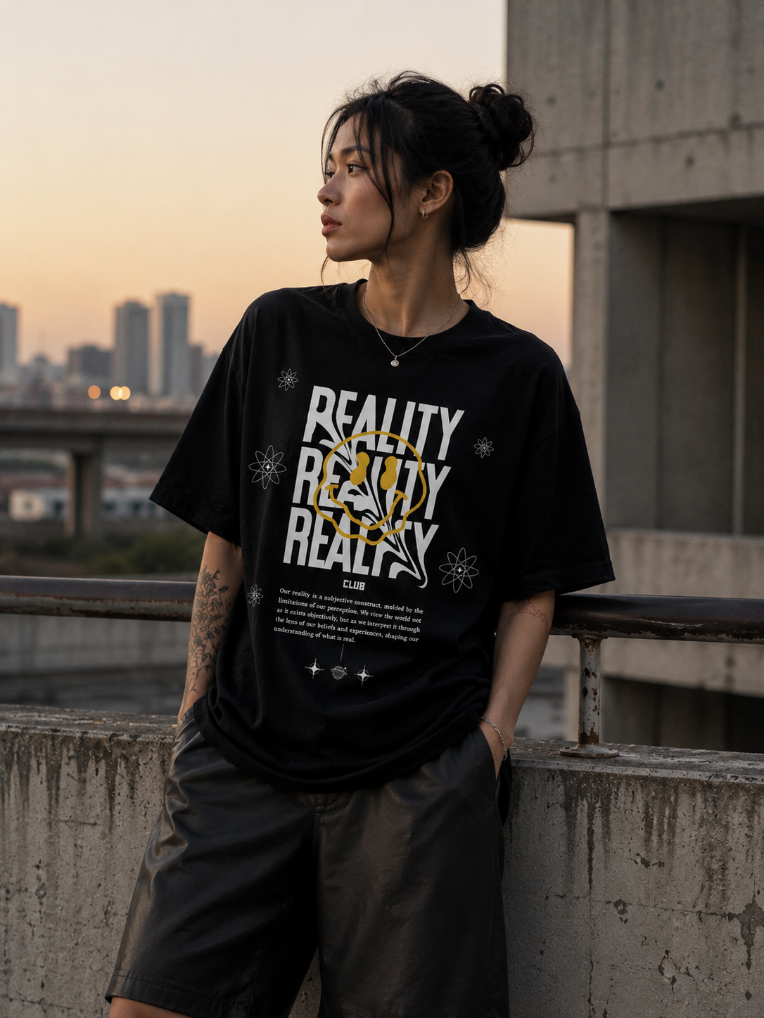 Person wearing a black t-shirt with 'REALITY' text, standing on a rooftop with cityscape in the background. Stylist streetwear tee, comfy formal tee, fashion tee, graphic tee