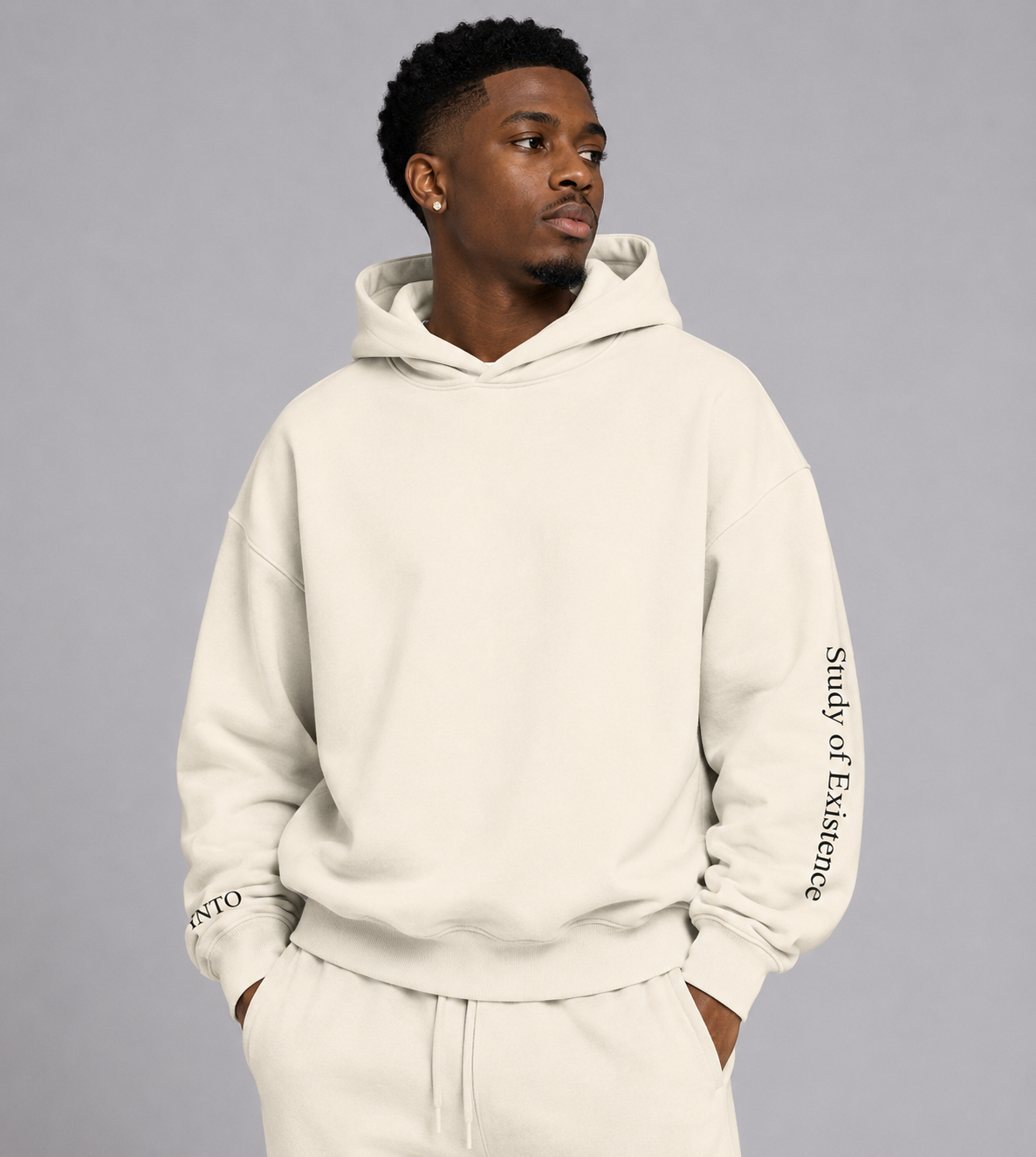 Man wearing a beige hoodie with text on sleeves against a gray background. Stylist streetwear hoodie, comfy formal hoodie, fashion hoodie, graphic hoodie, no front pocket hoodie, large hooded hoodie, large hood hoodie, oversized hoodie