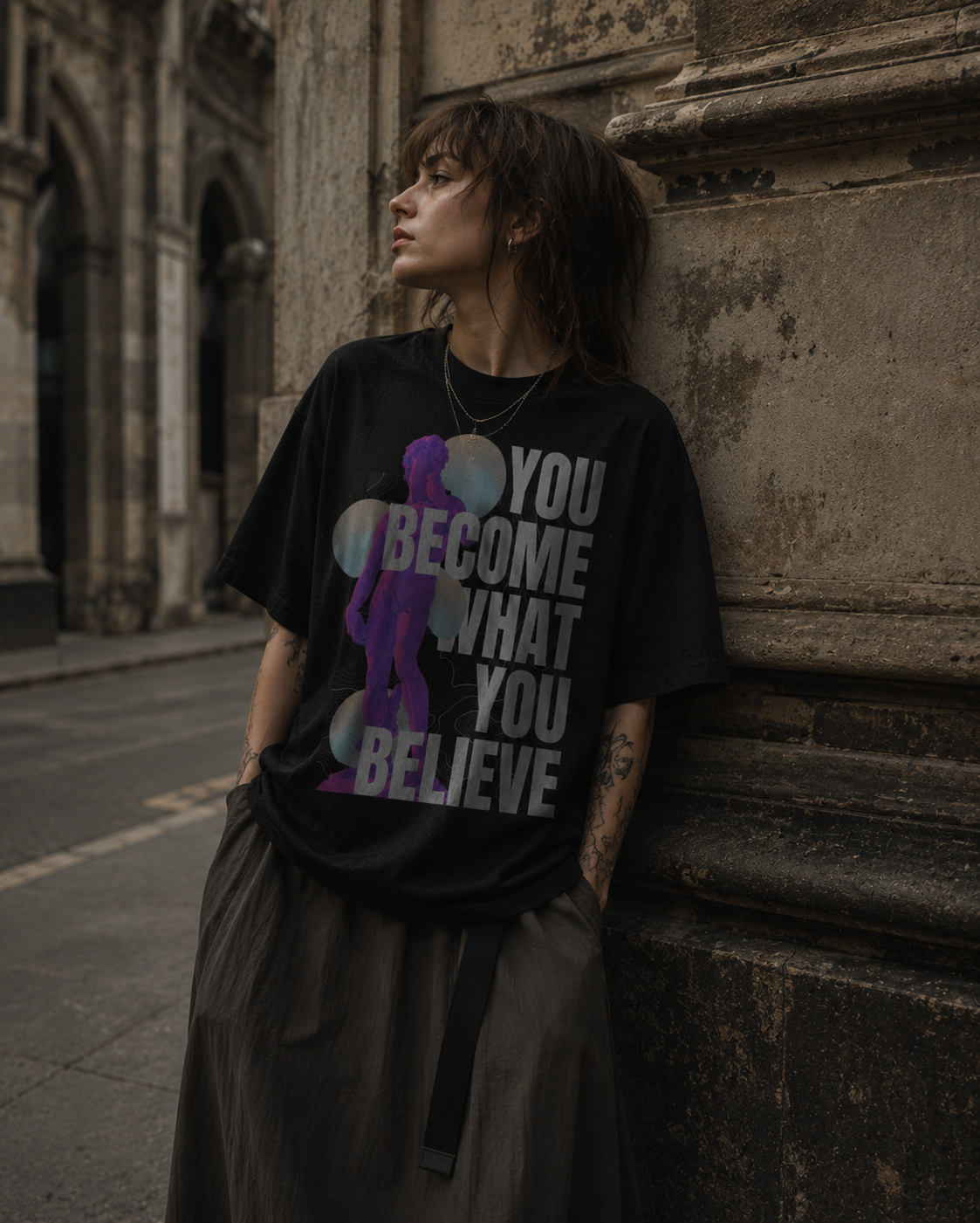 Person wearing a black t-shirt with a motivational quote, leaning against a stone wall. Stylist streetwear tee, comfy formal tee, fashion tee, graphic tee