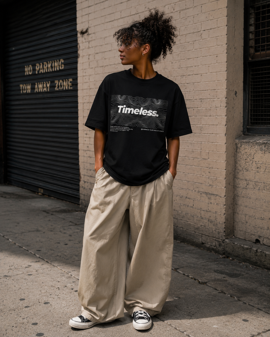 Person wearing a black t-shirt with 'Timeless' text against a brick wall. Stylist streetwear tee, comfy formal tee, fashion tee, graphic tee