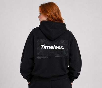 Person wearing a black hoodie with 'Timeless.' text on the back against a gray background. Stylist streetwear hoodie, comfy formal hoodie, fashion hoodie, graphic hoodie, no front pocket hoodie, large hooded hoodie, large hood hoodie, oversized hoodie