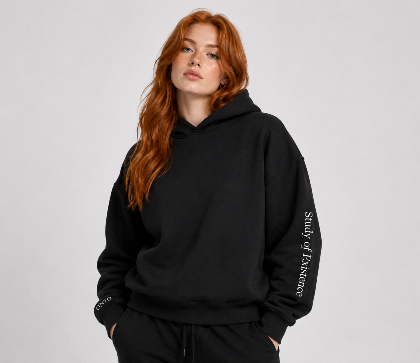 Person wearing a black hoodie with text on the sleeve against a plain background. Stylist streetwear hoodie, comfy formal hoodie, fashion hoodie, graphic hoodie, no front pocket hoodie, large hooded hoodie, large hood hoodie, oversized hoodie