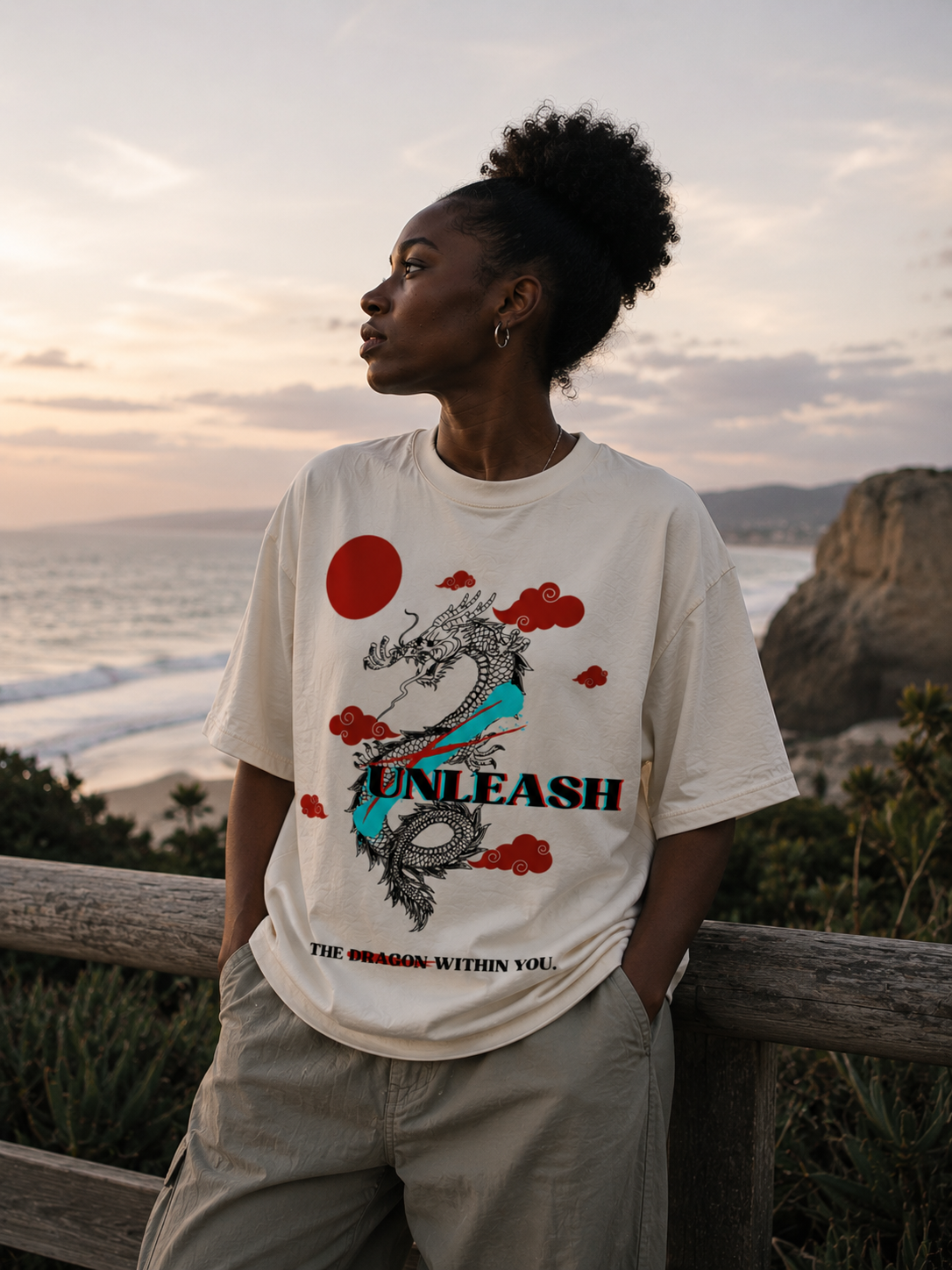 Person wearing a t-shirt with a dragon design and text, standing on a cliff overlooking the ocean. Stylist streetwear tee, comfy formal tee, fashion tee, graphic tee