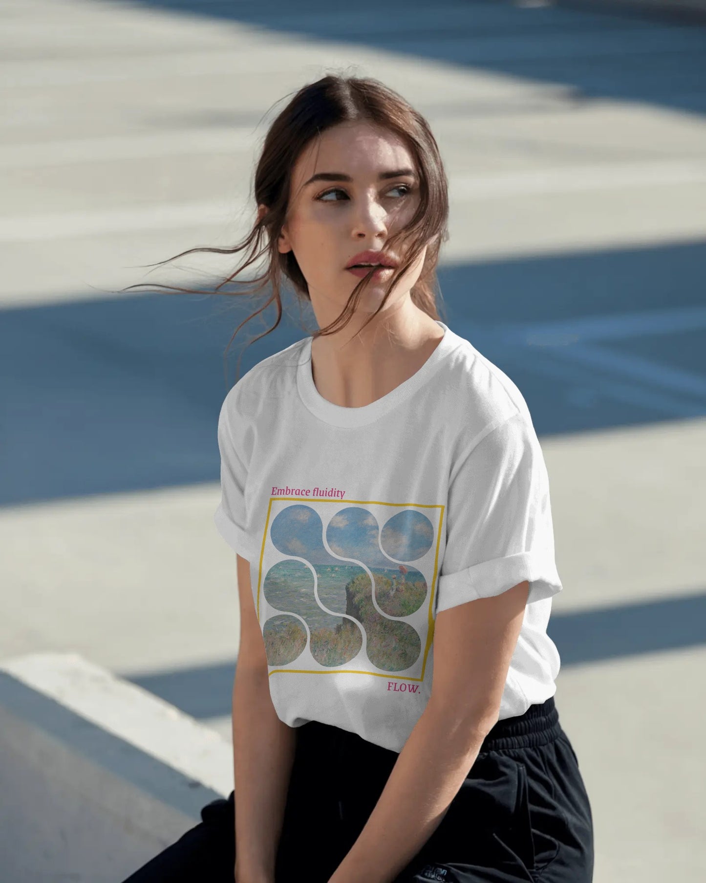 Woman wearing a white t-shirt with a graphic design sitting on a concrete surface.