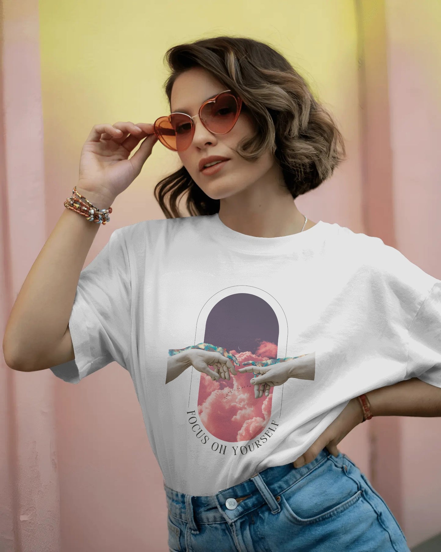 Woman wearing a white t-shirt with a graphic design, holding sunglasses against a colorful background.