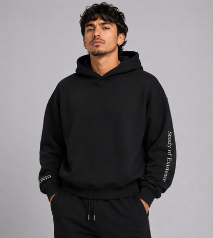 Man wearing a black hoodie with text on sleeves against a gray background. Stylist streetwear hoodie, comfy formal hoodie, fashion hoodie, graphic hoodie, no front pocket hoodie, large hooded hoodie, large hood hoodie, oversized hoodie