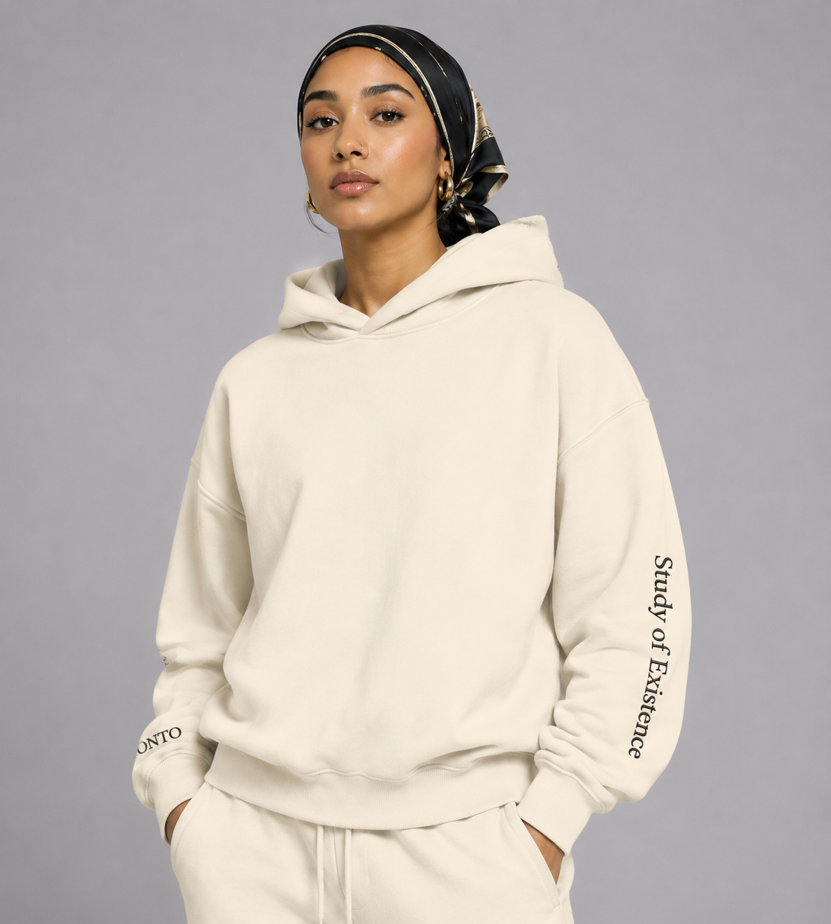 Person wearing a beige hoodie with text on the sleeve against a gray background. Stylist streetwear hoodie, comfy formal hoodie, fashion hoodie, graphic hoodie, no front pocket hoodie, large hooded hoodie, large hood hoodie, oversized hoodie