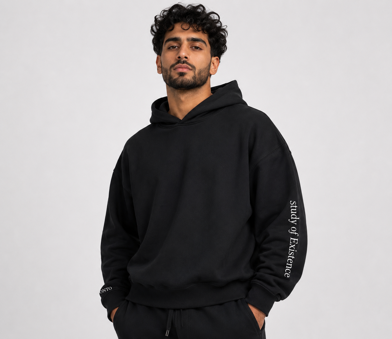 Man wearing a black hoodie with 'study of Existence' text on a gray background. Stylist streetwear hoodie, comfy formal hoodie, fashion hoodie, graphic hoodie, no front pocket hoodie, large hooded hoodie, large hood hoodie, oversized hoodie
