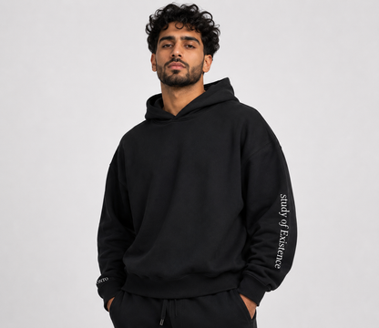 Man wearing a black hoodie with 'study of Existence' text on a gray background. Stylist streetwear hoodie, comfy formal hoodie, fashion hoodie, graphic hoodie, no front pocket hoodie, large hooded hoodie, large hood hoodie, oversized hoodie